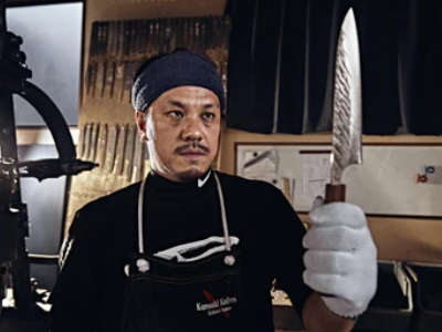 A portrait photo of Yu Kurosaki inspecting one of his gyuto knives in his workshop