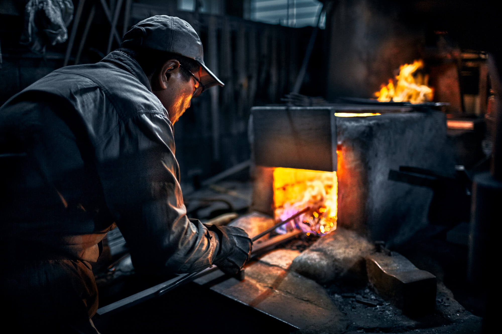 A blacksmith from Sakai Takayuki  working with hot metal in a forge with flames and smoke.